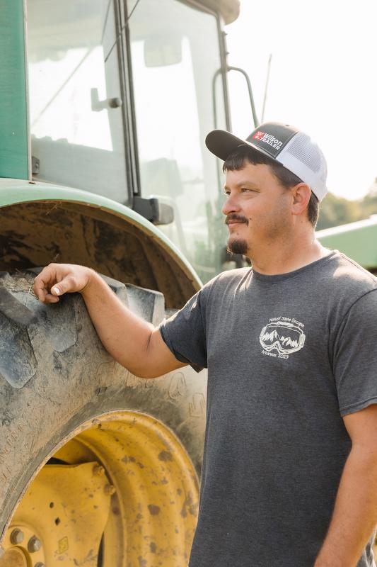 Man stands next to tractor tire looking into the distance