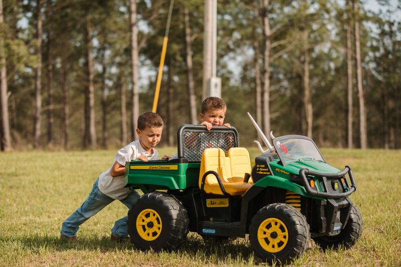 Two young boys outside pushing a kids' ride-on John Deere gator