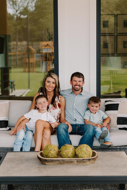Greene family sits on an outdoor couch in front of home windows
