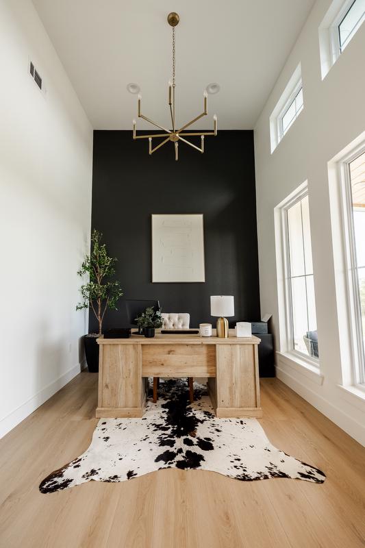 Narrow office area with a lot of natural light, dark accent wall, gold chandelier, cowhide rug