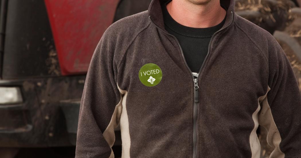 Close up of person in fleece jacket in front of a tractor with green "I VOTED" sticker on their jacket