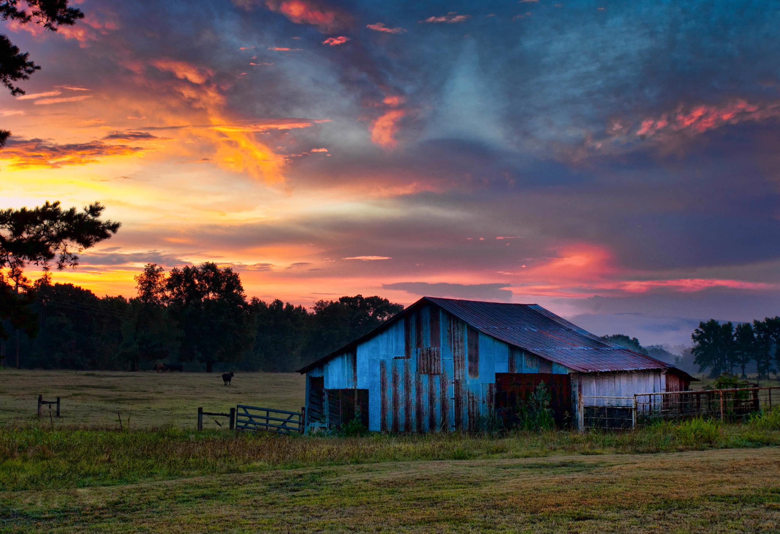 Rusted metal barn in front of red, orange, pink, and blue sunset.