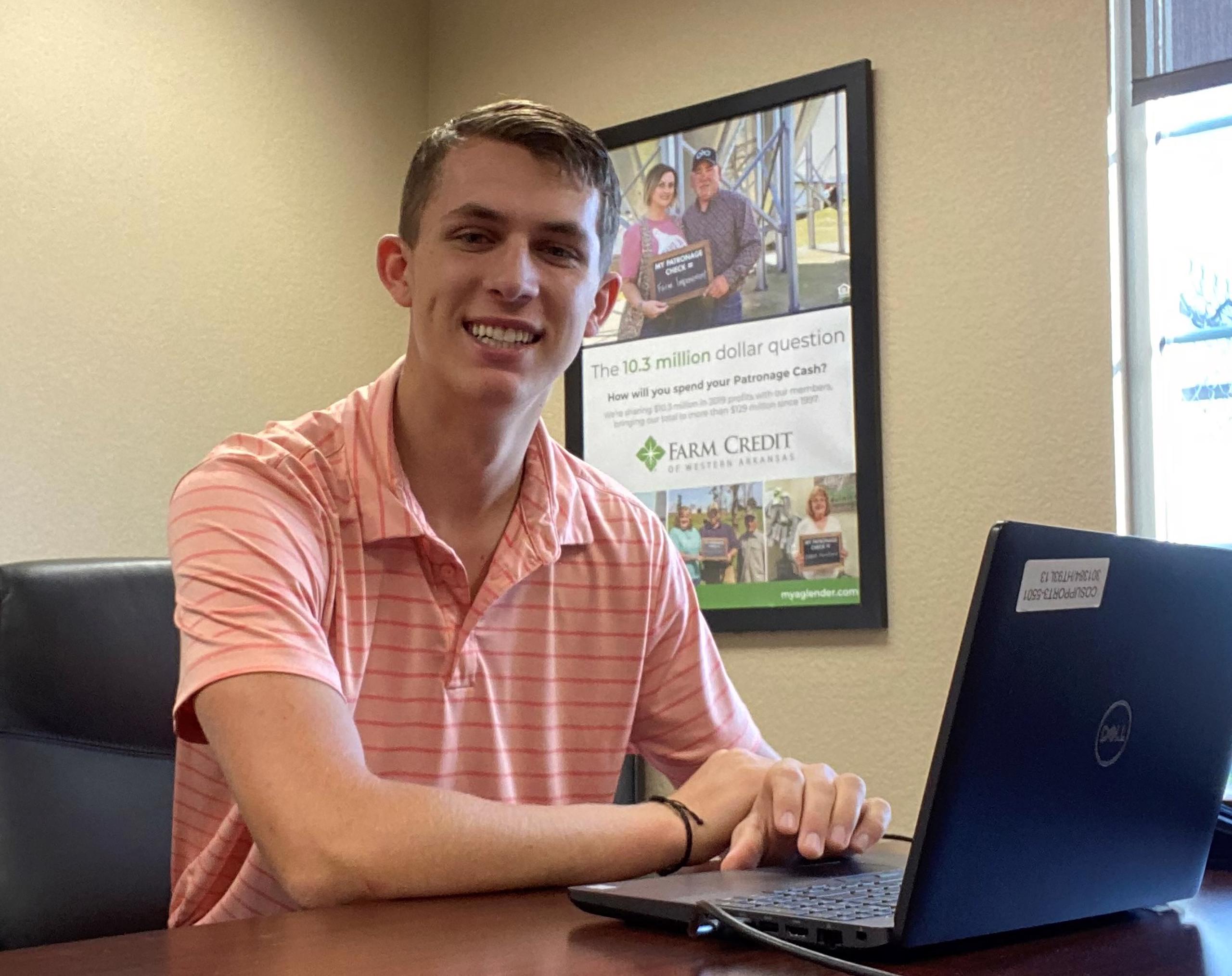 Colton Hewitt, Field Services Inter, sits at a desk and smiles toward camera