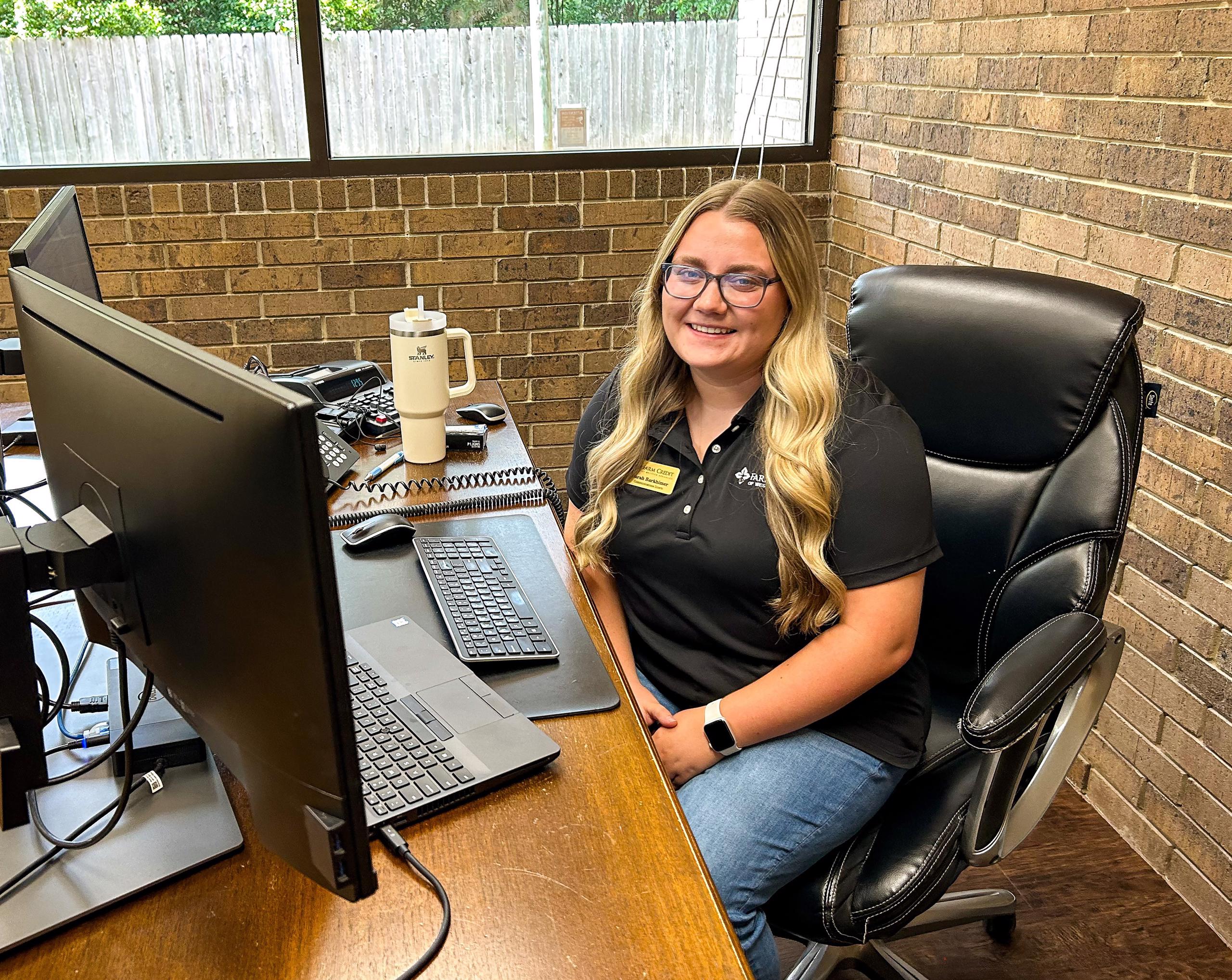 Sarah Barkhimer, Communications Intern, sits at desk and smiles to camera